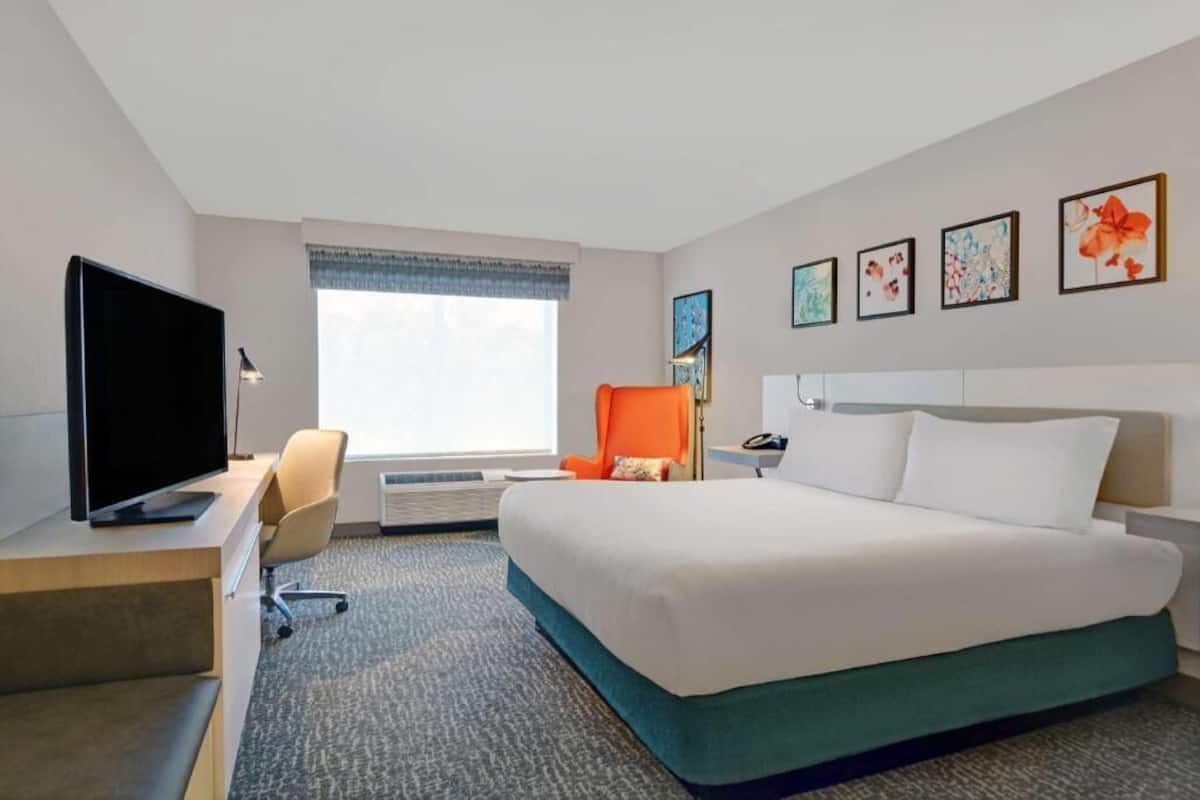 Une chambre d’hôtel avec un lit, un bureau avec une télévision, une chaise et des œuvres d’art encadrées accrochées au mur.