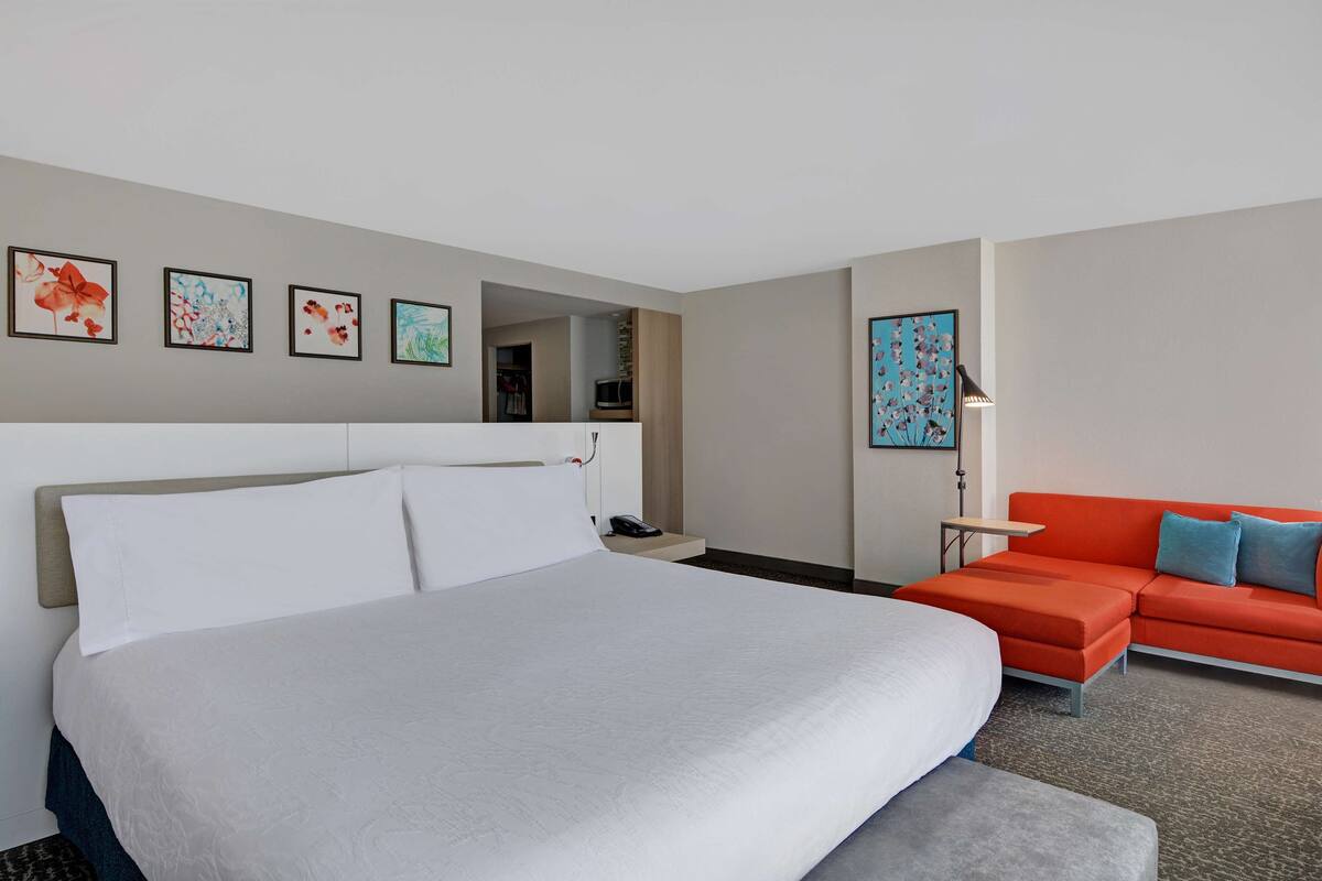 Une chambre d’hôtel avec un grand lit, un canapé et un bureau. Quatre œuvres d’art encadrées ornent le mur.