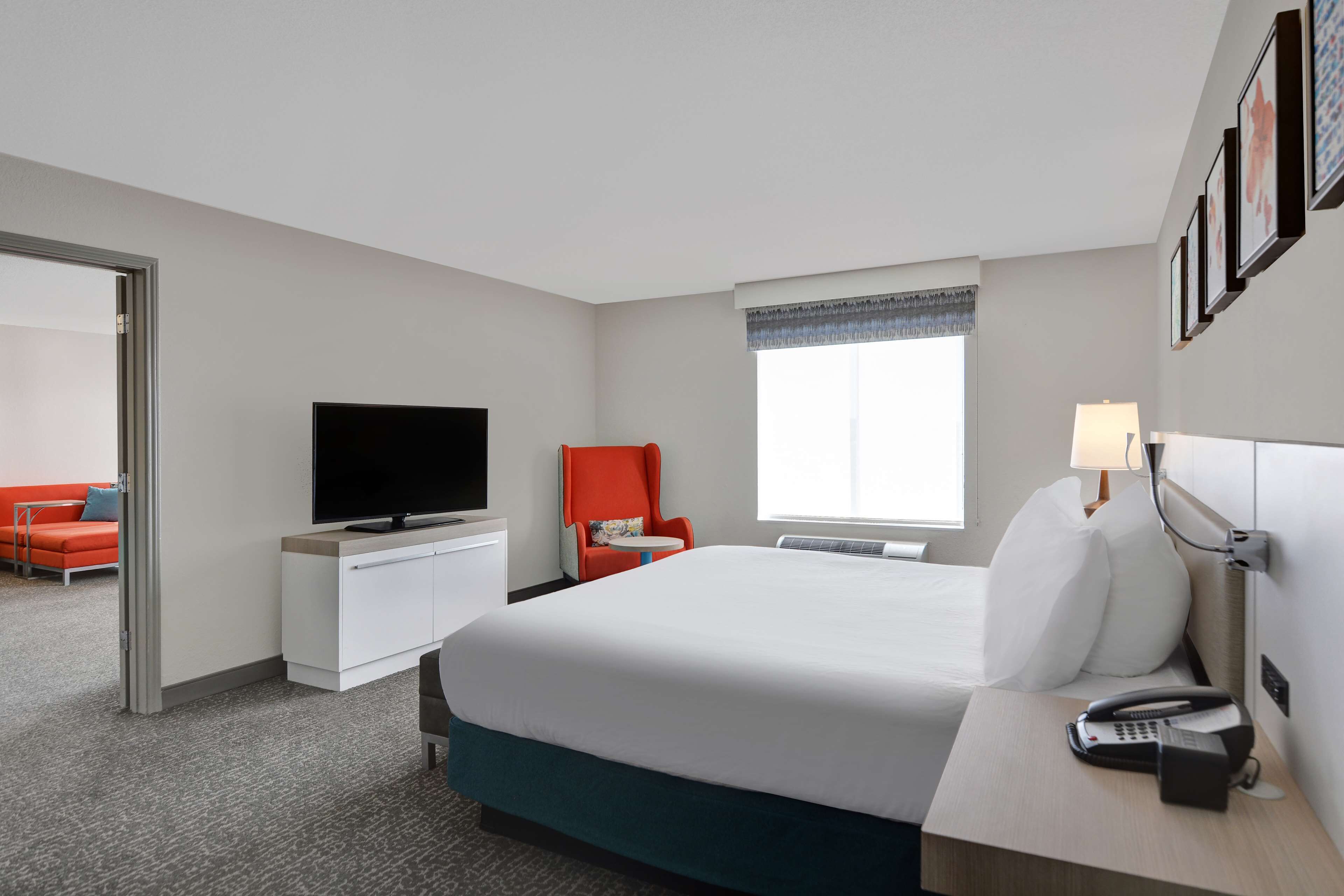 A hotel room with a bed, a TV, a desk with a lamp, a phone, and a window with a view.