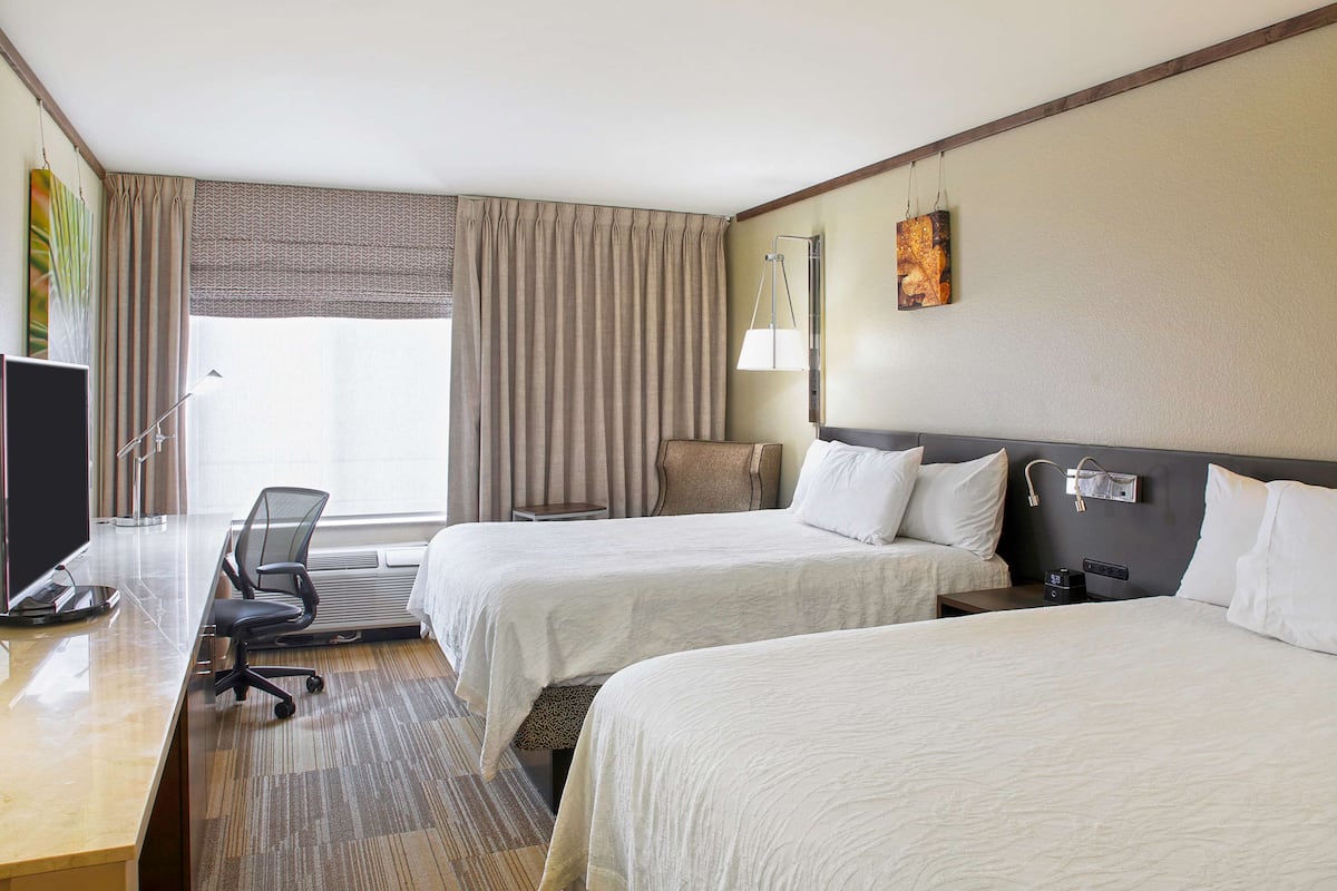 Une chambre d’hôtel avec deux lits, un bureau, une chaise et une télévision.