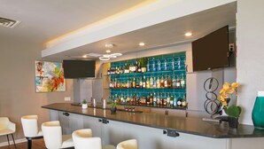A bar area with a long counter, multiple seating options, and a wall-mounted TV. - Hilton Garden Inn Bentonville Rogers (Bentonville)