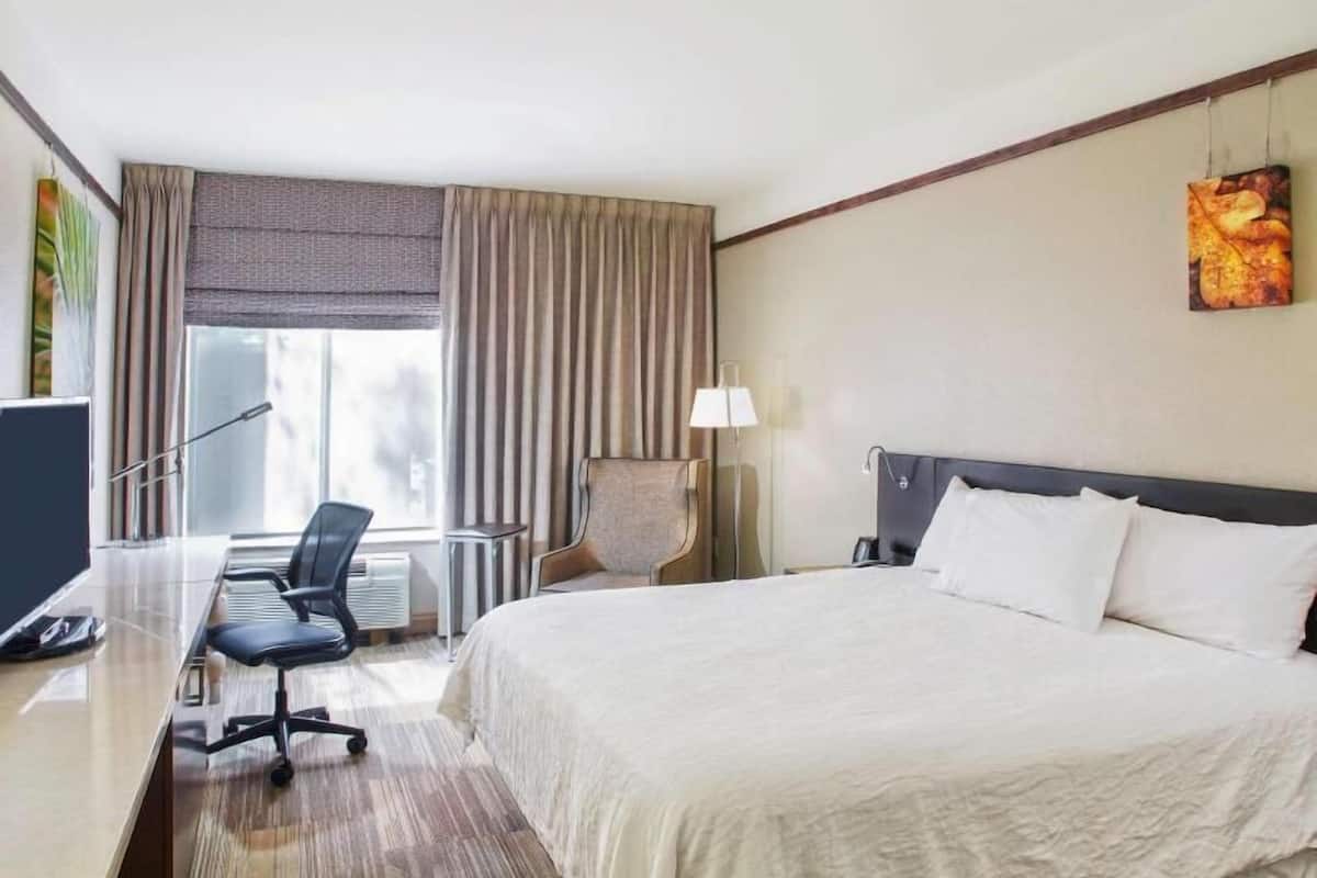 Une chambre d’hôtel avec un grand lit, un bureau avec une chaise, une lampe et une fenêtre avec des rideaux.