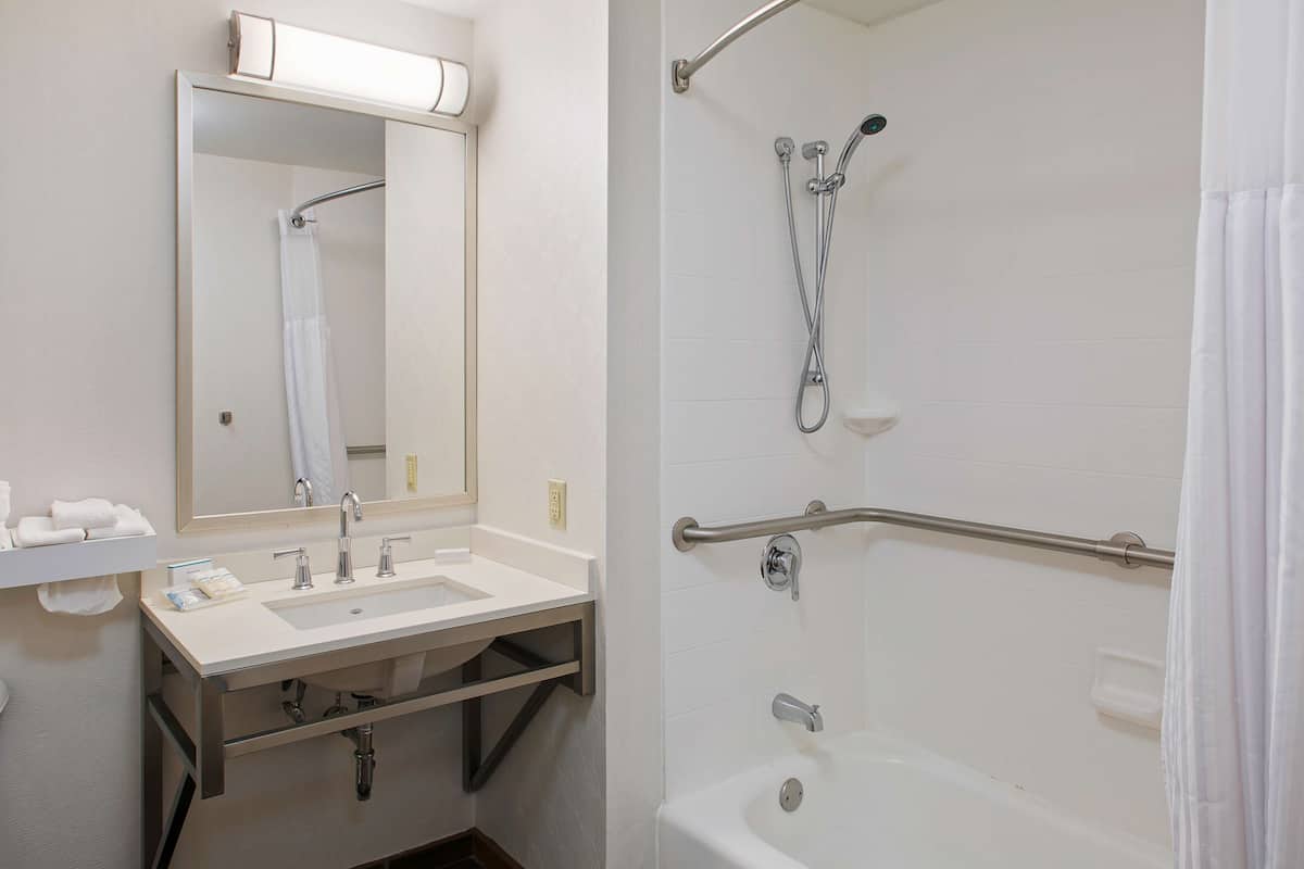 Une salle de bain équipée d’un lavabo, d’un miroir et d’une douche avec des barres d’appui.