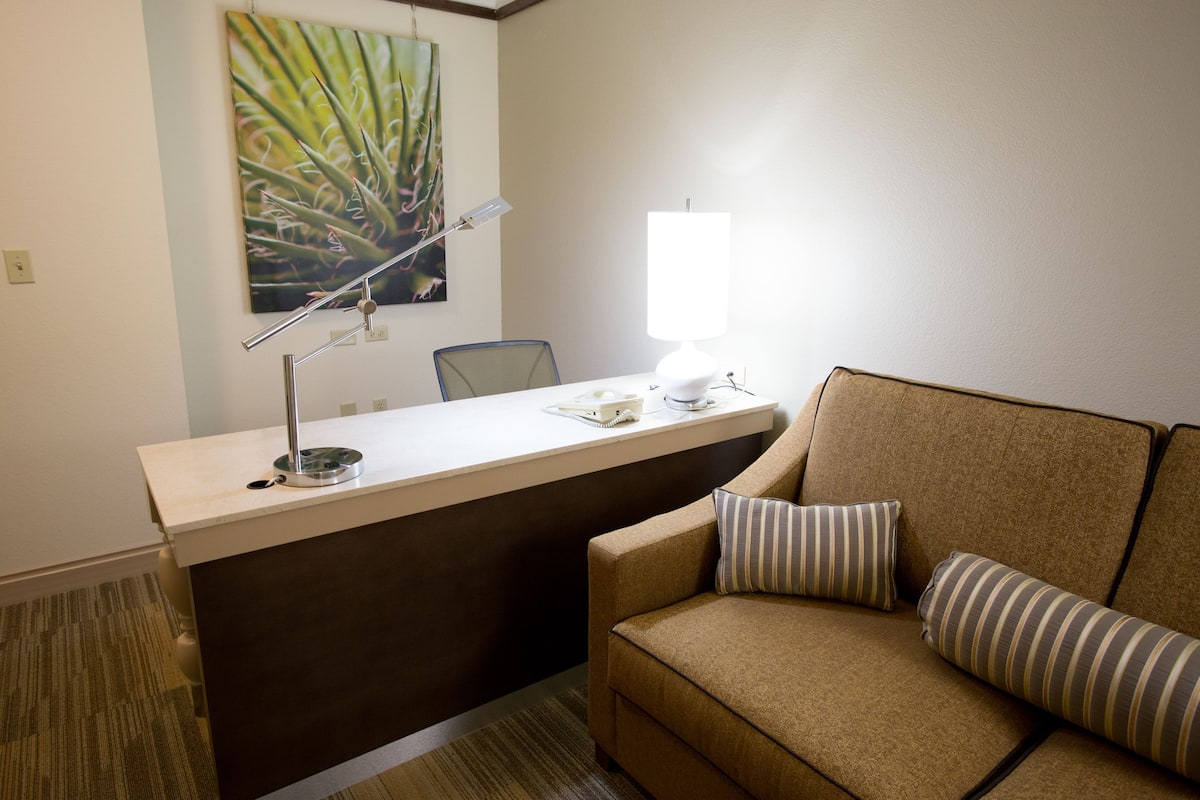 Une pièce comprenant un bureau, une chaise, un canapé, une lampe et un tableau accroché au mur.
