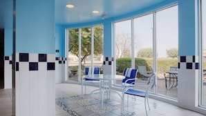A sunlit indoor patio with a glass table and chairs, a tiled floor, and a view of the outdoors. - Hilton Garden Inn Bentonville Rogers (Bentonville)