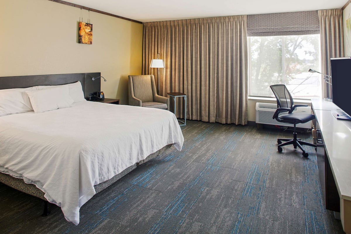 A hotel room with a bed, a desk, a chair, a lamp, and a window with curtains.