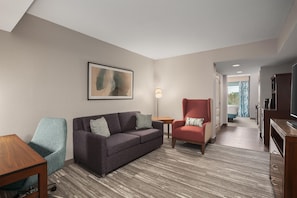 Een hotelkamer met een bank, fauteuil en een klein tafeltje. Aan de muur hangt een schilderij en op een bijzettafeltje staat een lamp.