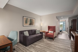 Ein Hotelzimmer mit einer Couch, einem Sessel und einem kleinen Tisch. An der Wand hängt ein Gemälde und auf einem Beistelltisch steht eine Lampe.