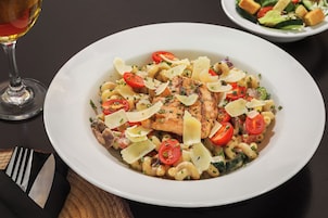 Un plato de pasta con salmón, tomates cherry y queso sobre una mesa.