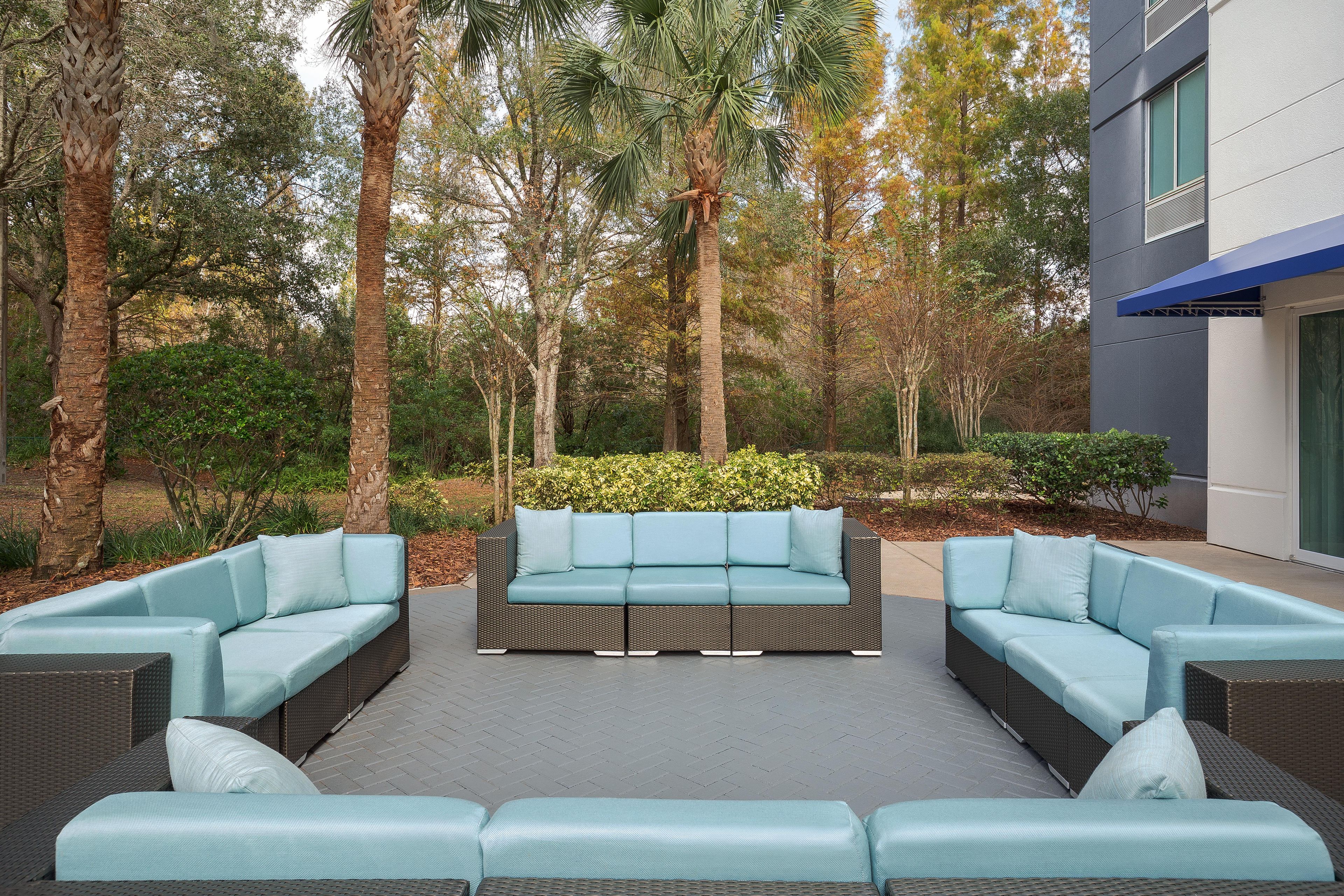 An outdoor seating area with a modern sofa set and a dining table, surrounded by trees and a hedge.