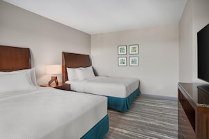 Una habitación de hotel con dos camas, un televisor y una pared decorada con cuatro cuadros.