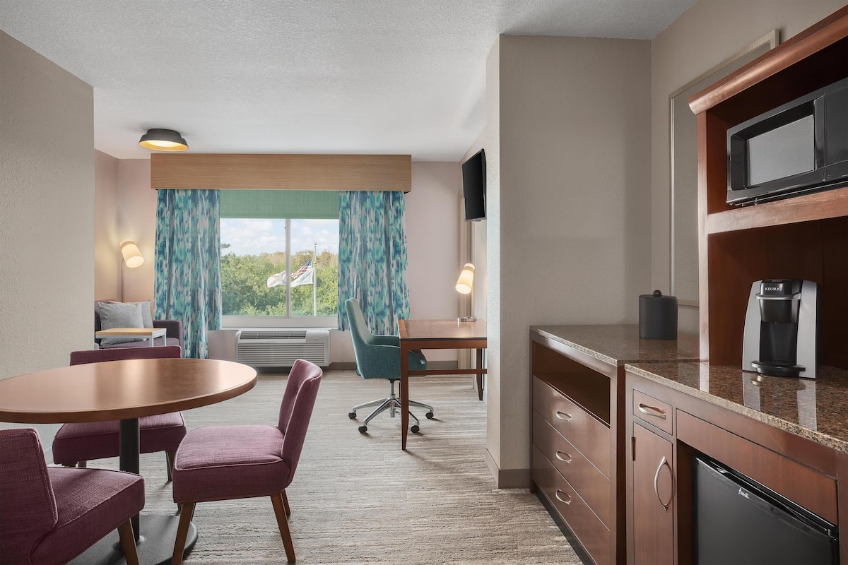 Habitación de hotel compacta con comedor, kitchenette y zona de estar con vistas al exterior.