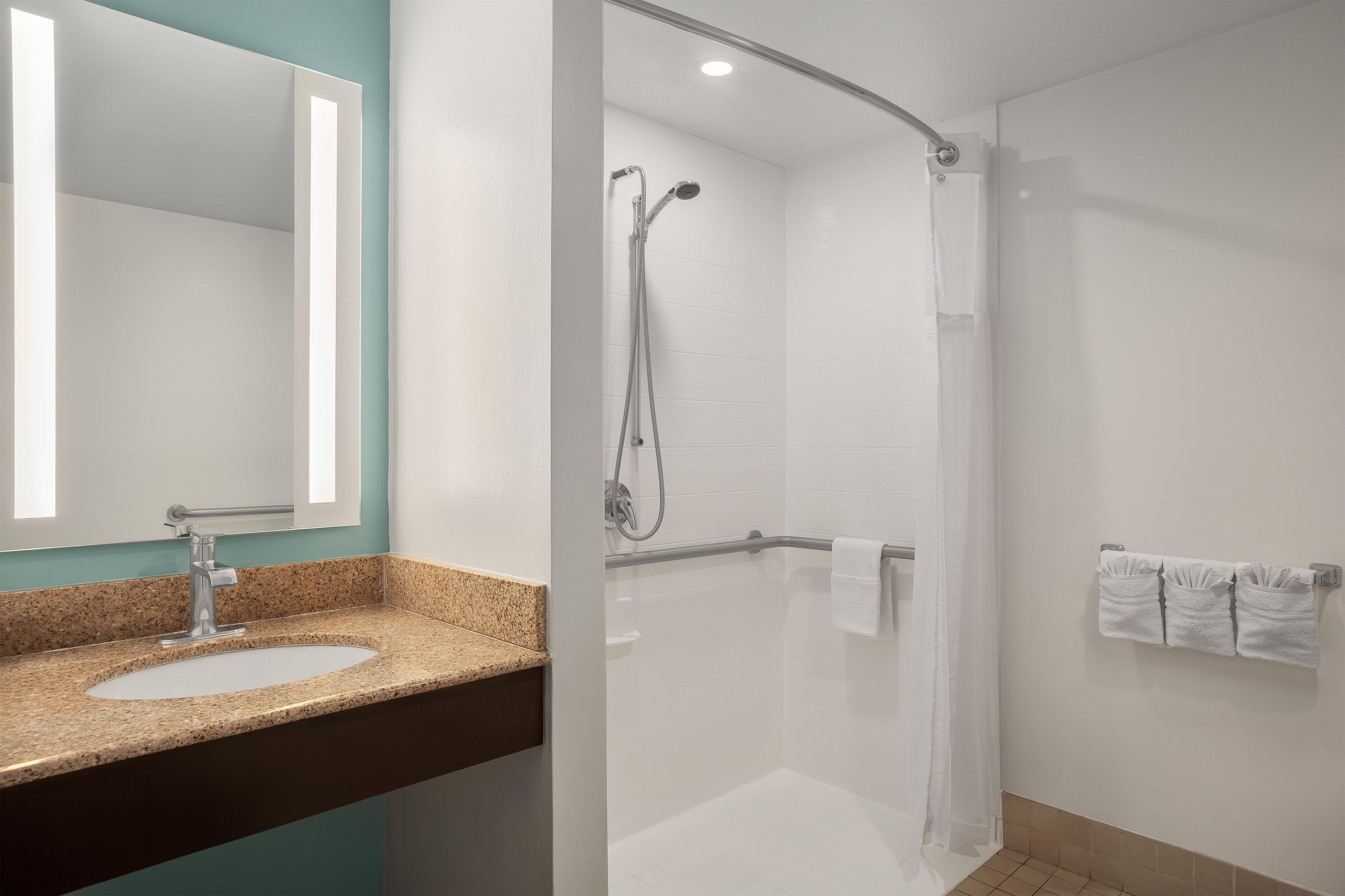 Un baño moderno con encimera de granito, cabina de ducha con paredes de vidrio y un perchero con varias toallas.