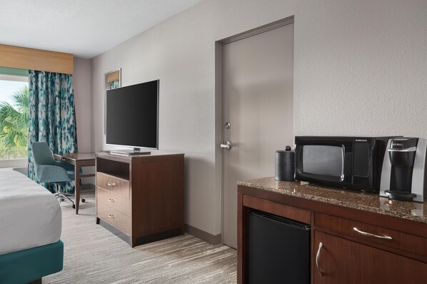 A hotel room with a bed, a desk, a television, a coffee maker, and a microwave.