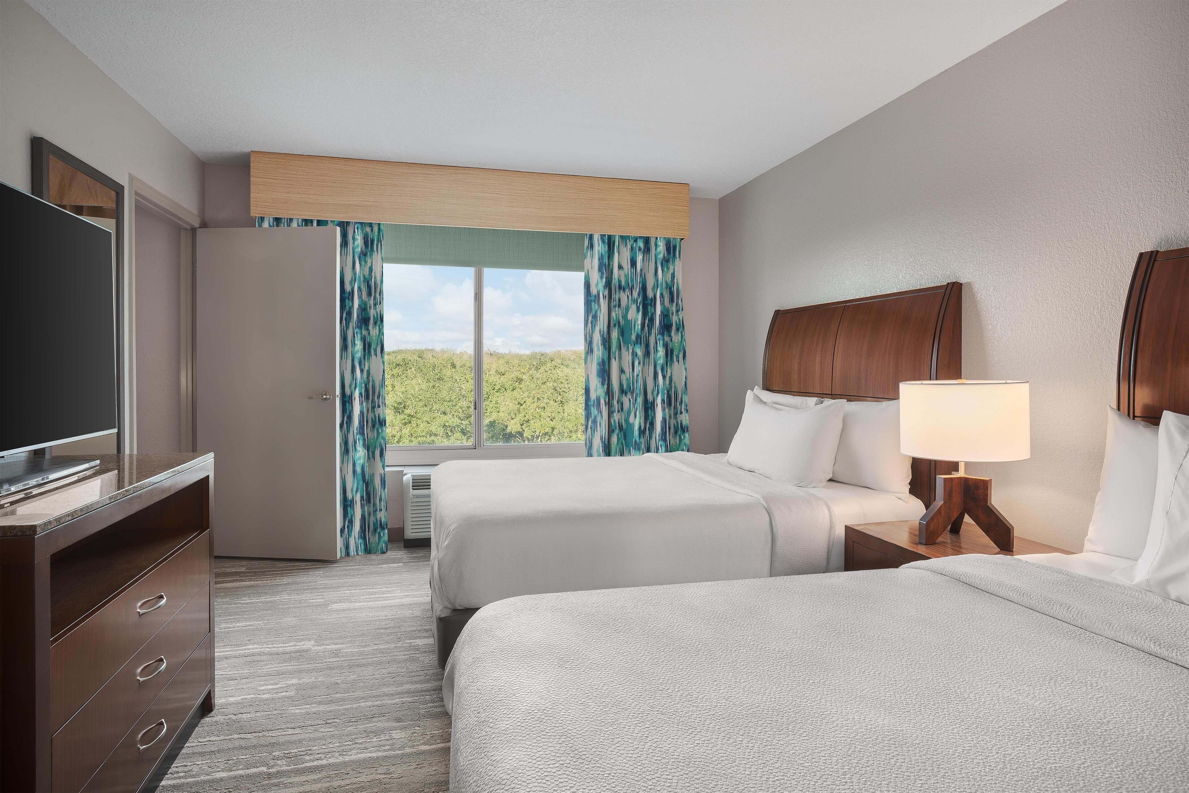 A hotel room with two beds, a TV, a desk, and a window with curtains.