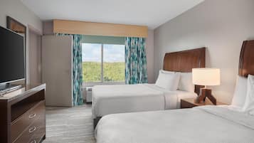 A hotel room with two beds, a TV, a desk, and a window with curtains.