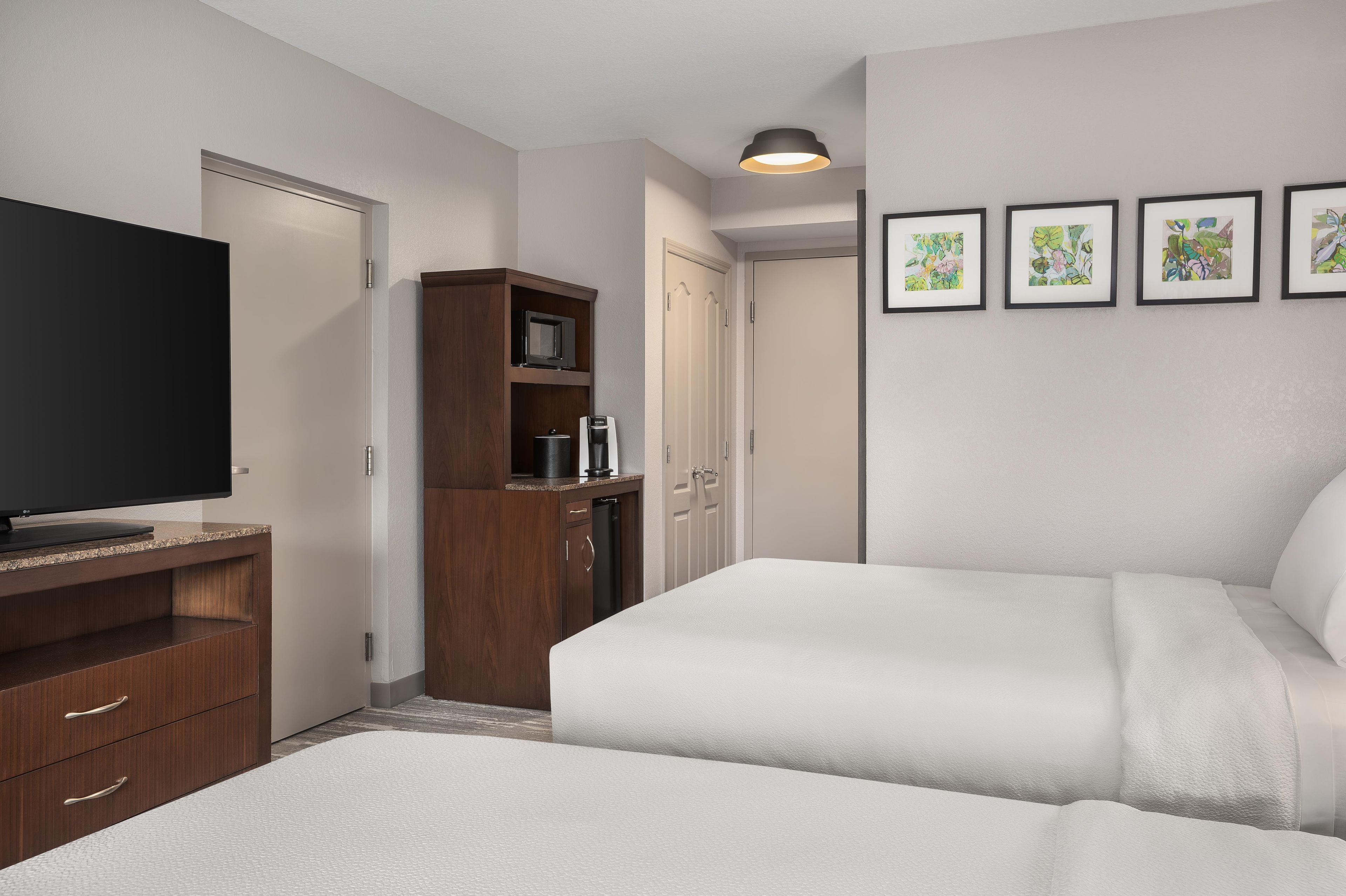 A hotel room with a bed, a TV, a minibar, a wardrobe, and a door leading to another room.