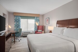 A hotel room with a bed, desk, chair, and a television.