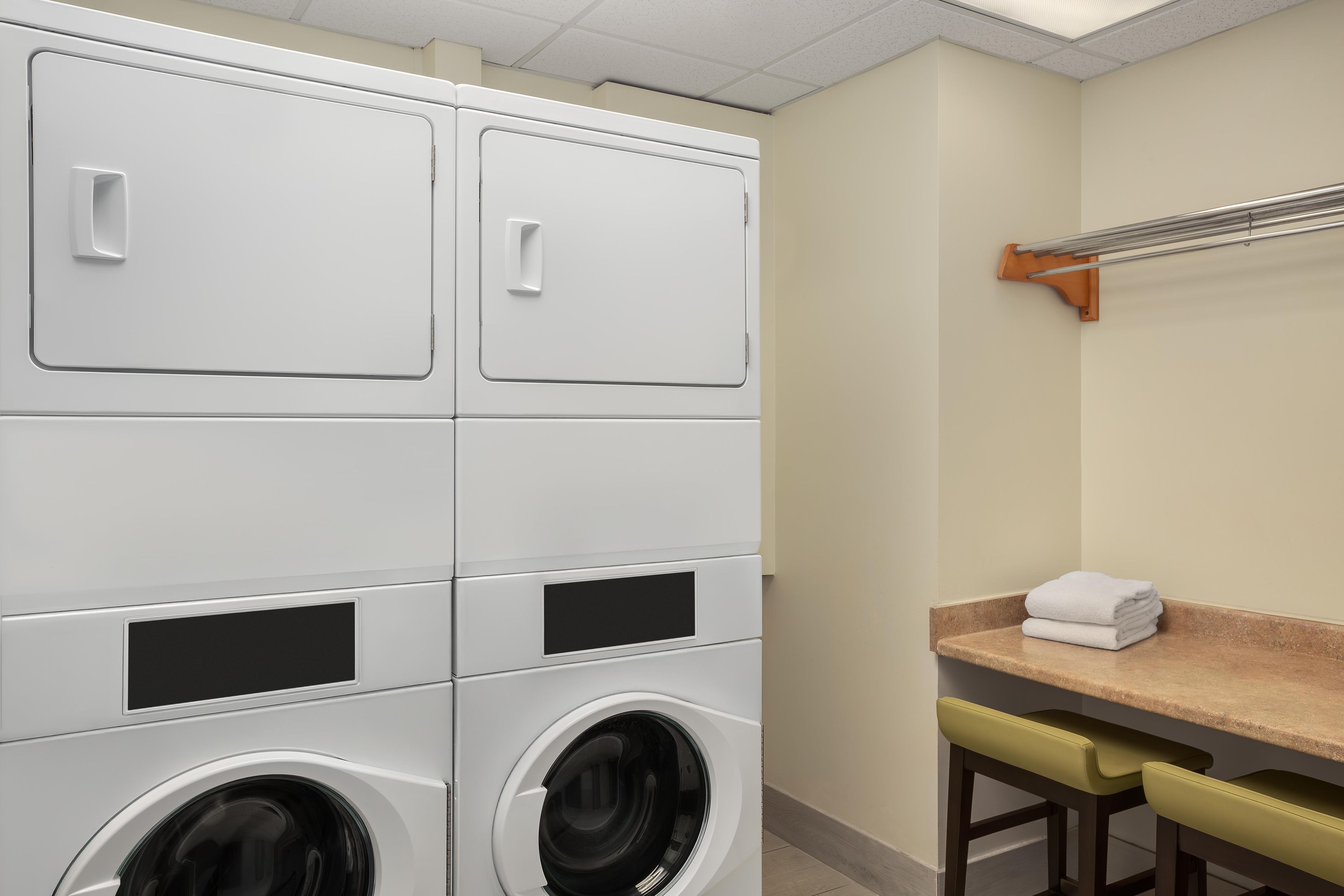 A laundry room with stacked washers and dryers, a towel rack, and a small table with towels.