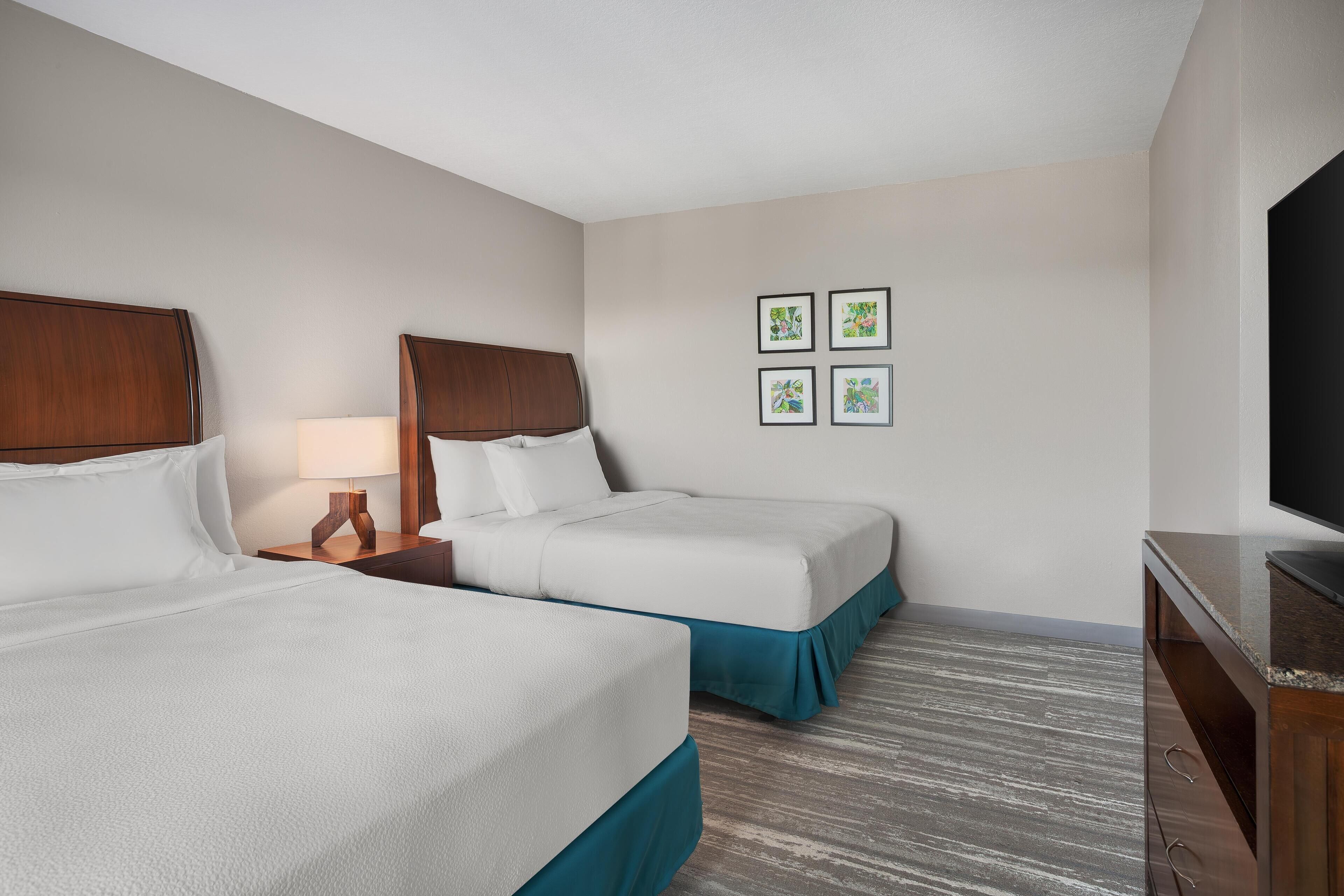 Quarto de hotel com duas camas, uma televisão e uma mesa de cabeceira com abajur.