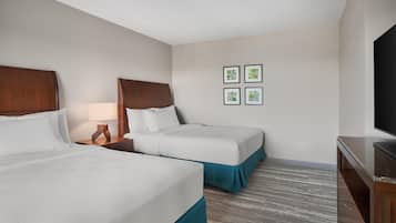 Quarto de hotel com duas camas, uma televisão e uma mesa de cabeceira com abajur.