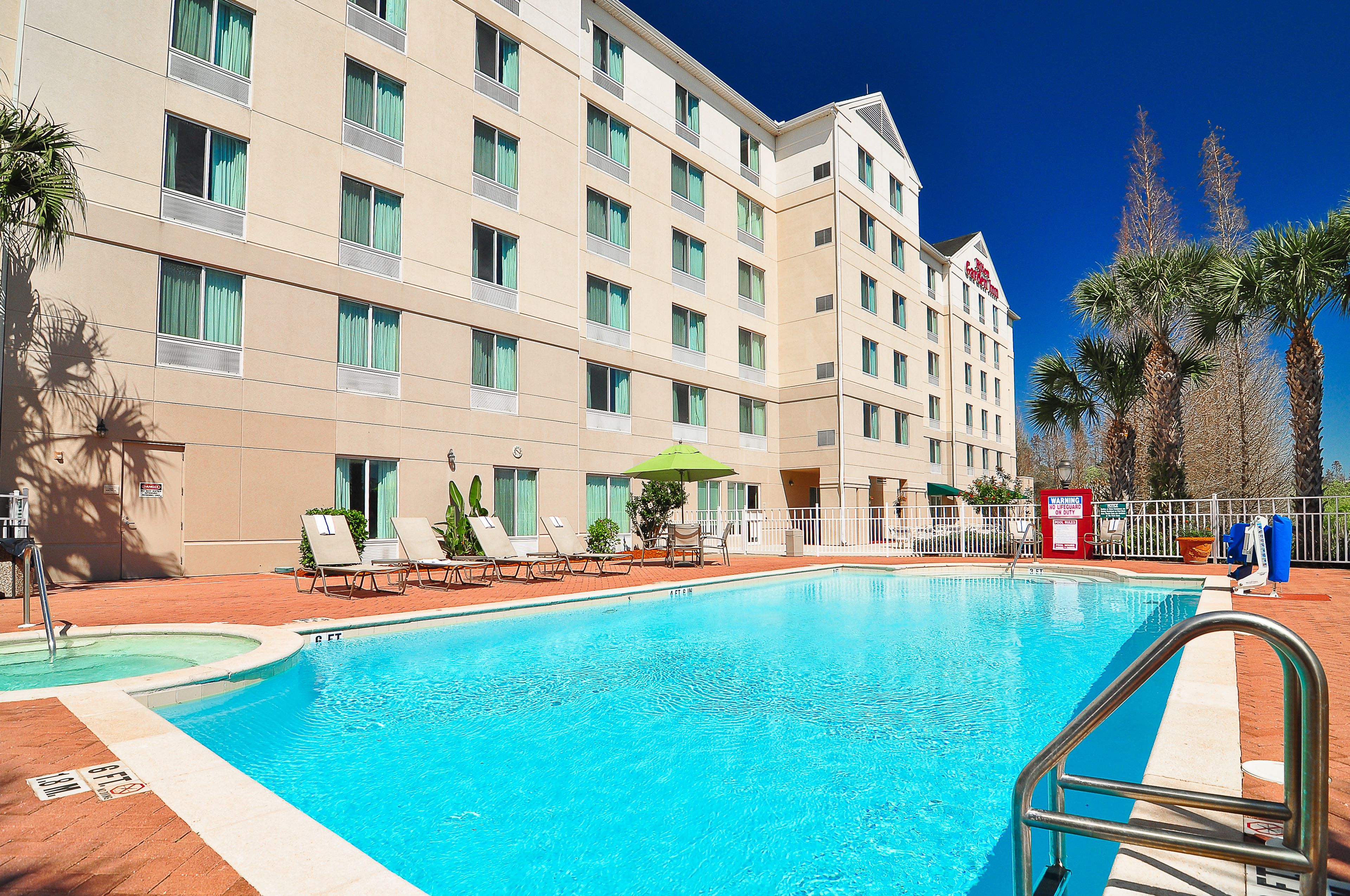 Een hotel met een zwembad, ligbedden en palmbomen.