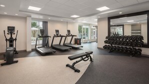 Un gimnasio con cintas de correr, elíptica, banco y estantería con mancuernas.