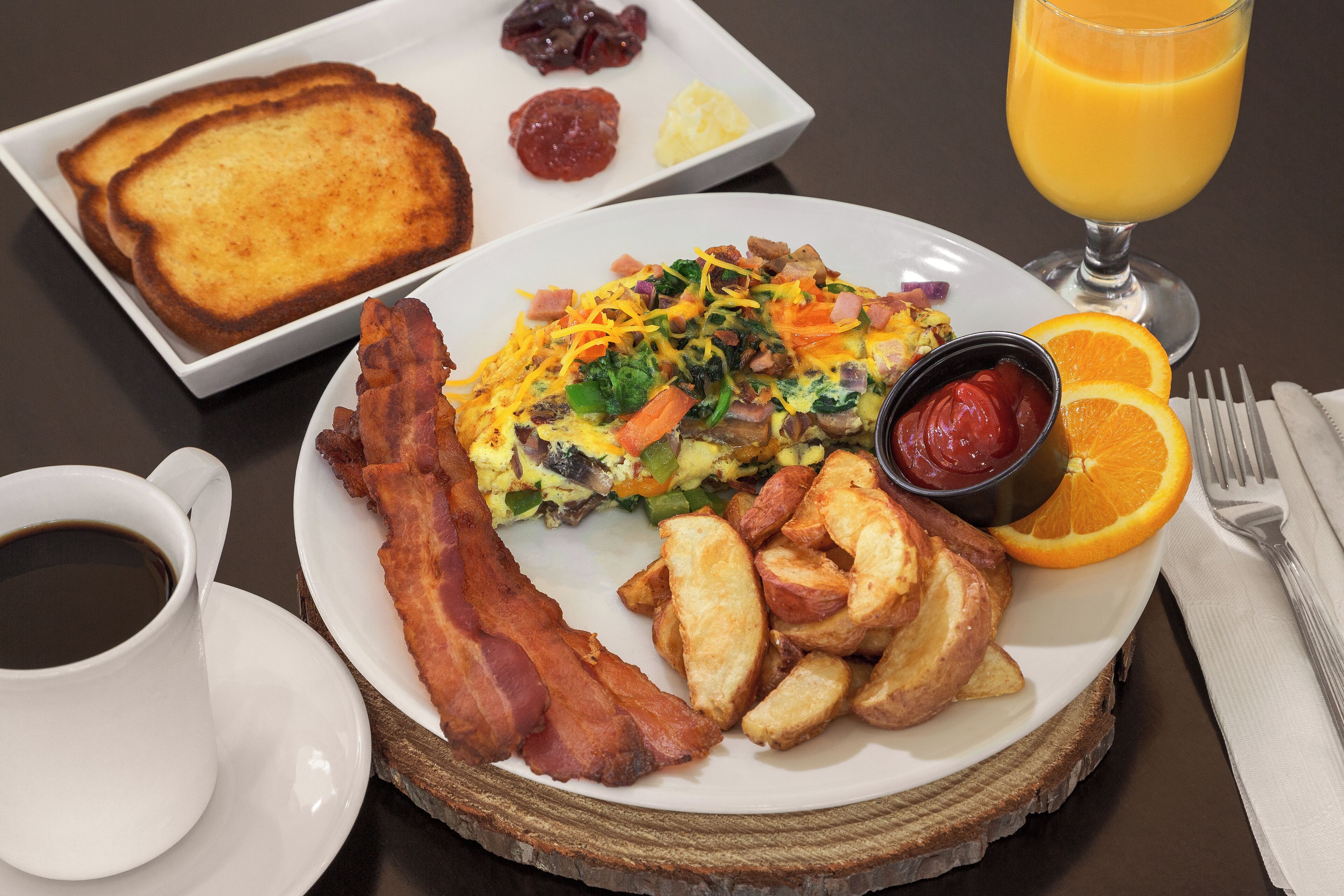 A breakfast plate with toast, bacon, potatoes, scrambled eggs, and a glass of orange juice.