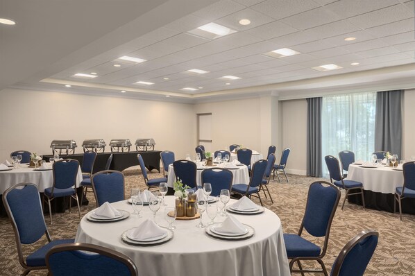 Une salle de conférence avec des tables rondes, des chaises bleues et des nappes blanches.