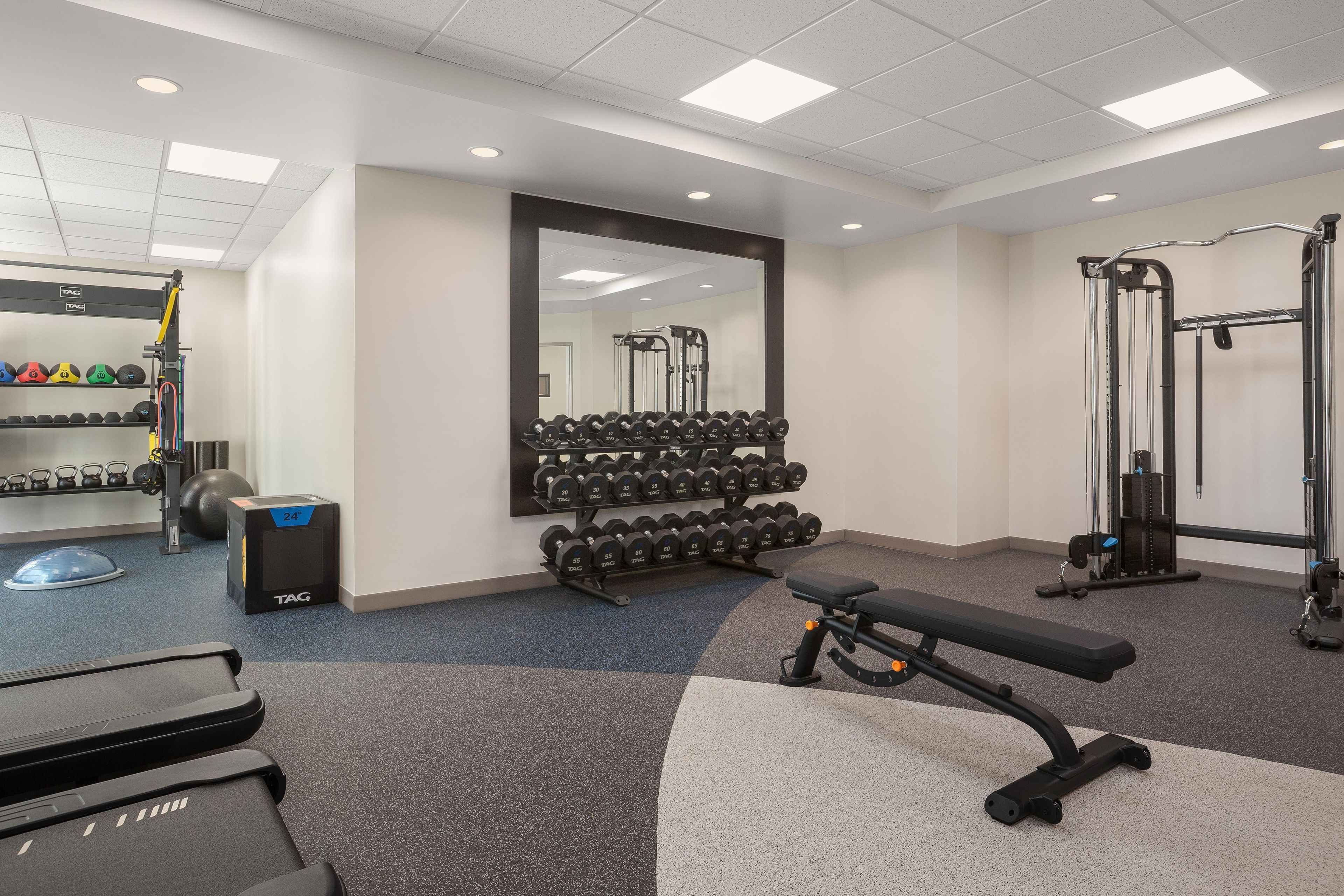 Une salle de sport équipée de matériel d’exercice, notamment des haltères, un banc et un tapis de course.
