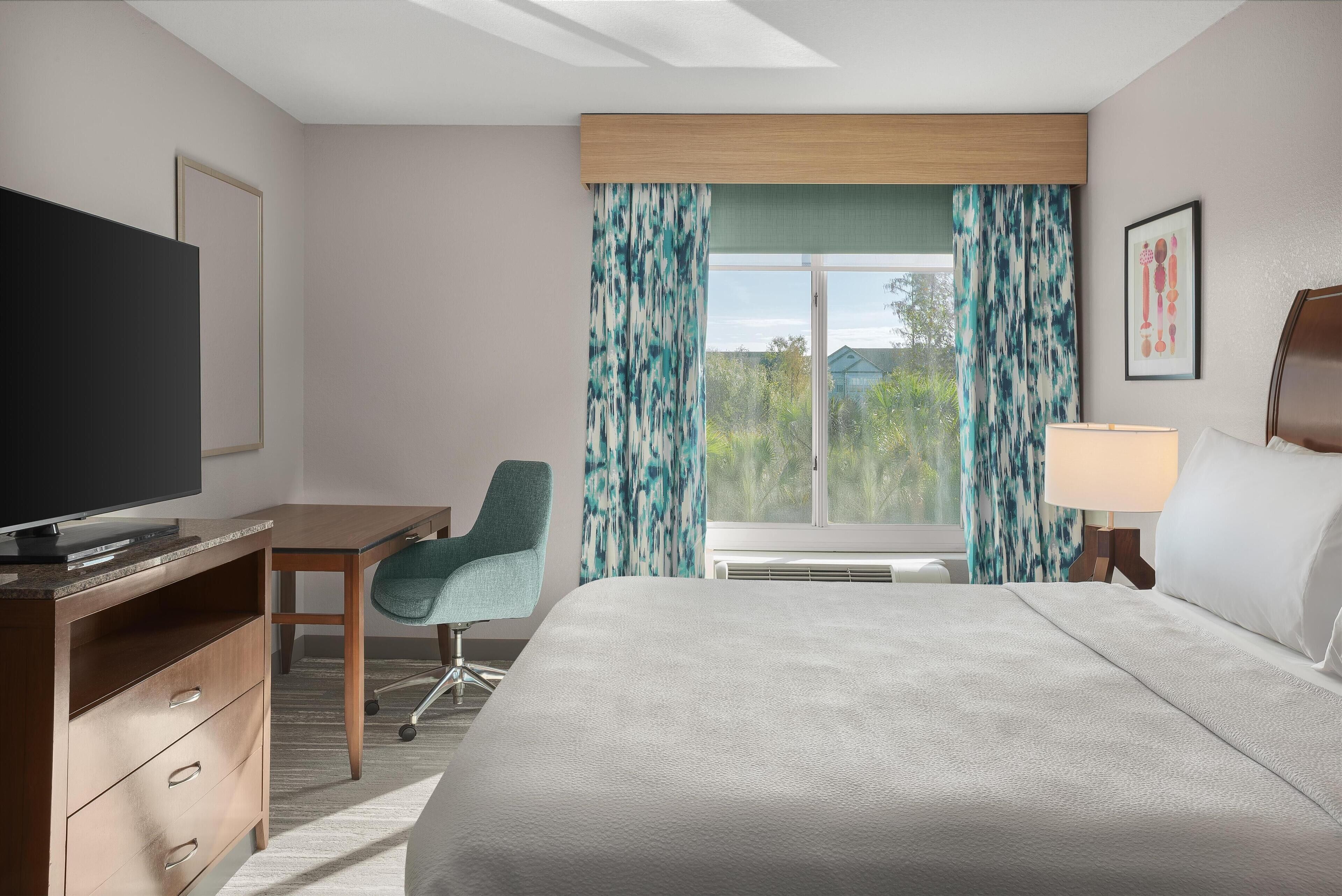 A hotel room with a bed, a desk, a television, and a window with curtains.