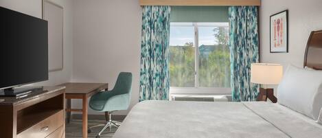 A hotel room with a bed, a desk, a television, and a window with curtains.