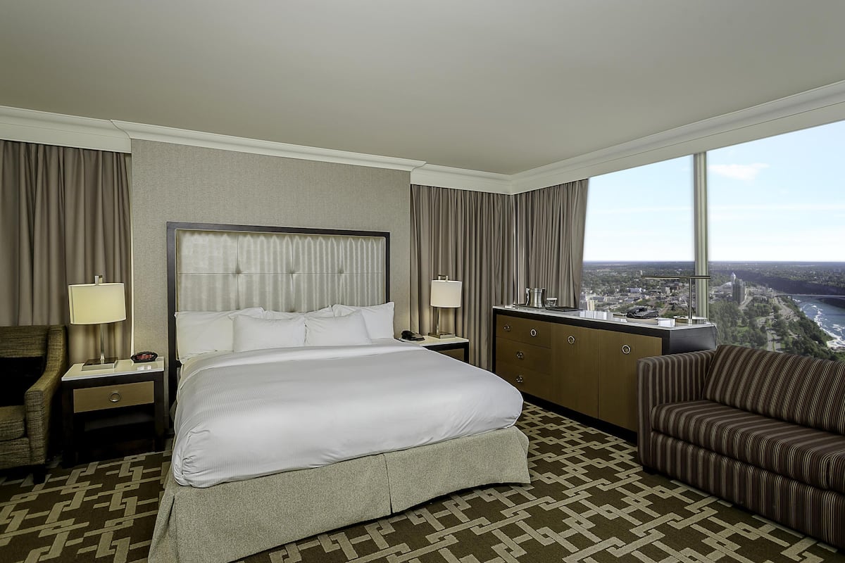Une chambre d’hôtel avec un grand lit, un bureau, une chaise, une commode et une vue sur le paysage urbain.