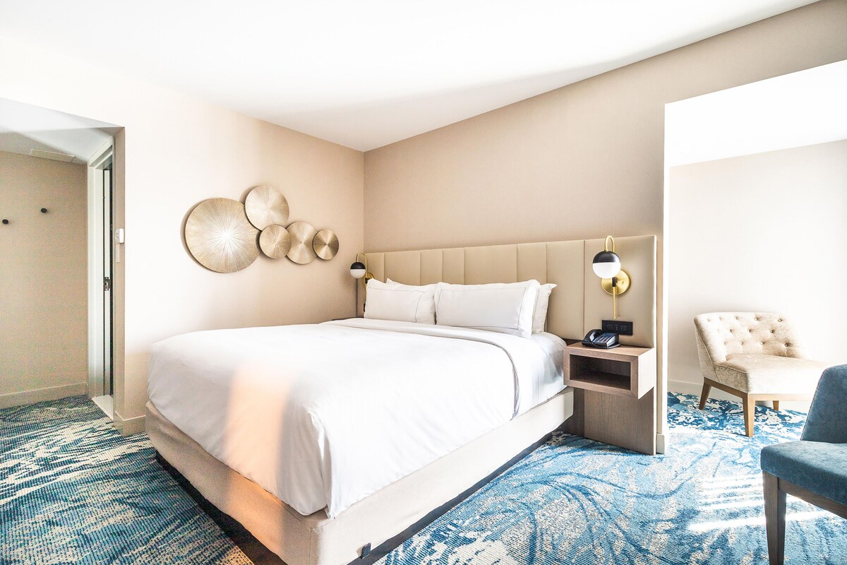 A hotel room with a large bed, a nightstand, a chair, and wall decor.