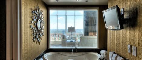 A modern bathroom with a large bathtub, a vanity with a mirror, and a television mounted on the wall.