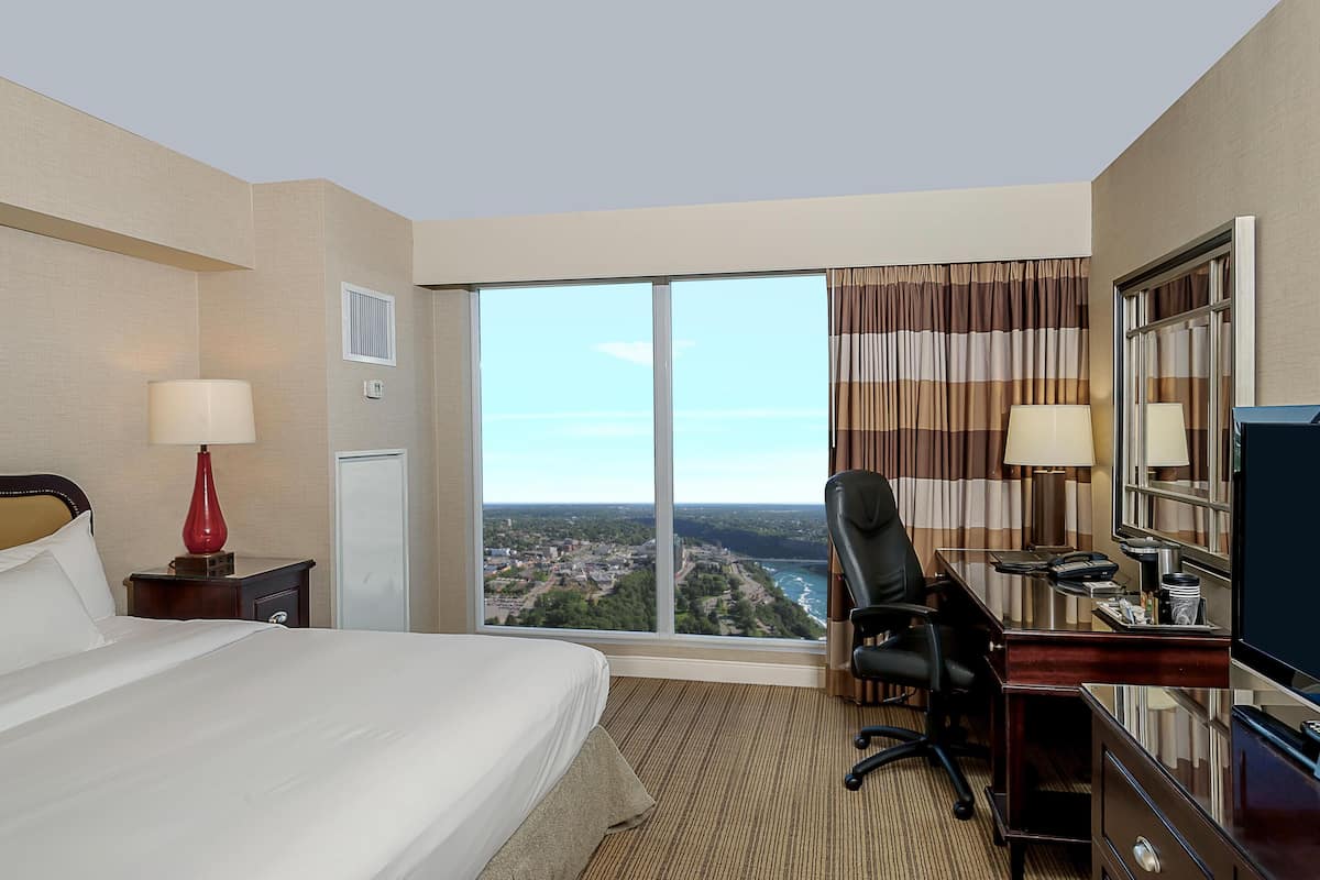 Une chambre d’hôtel avec un grand lit, un bureau avec une chaise, une télévision et une vue sur le paysage urbain.