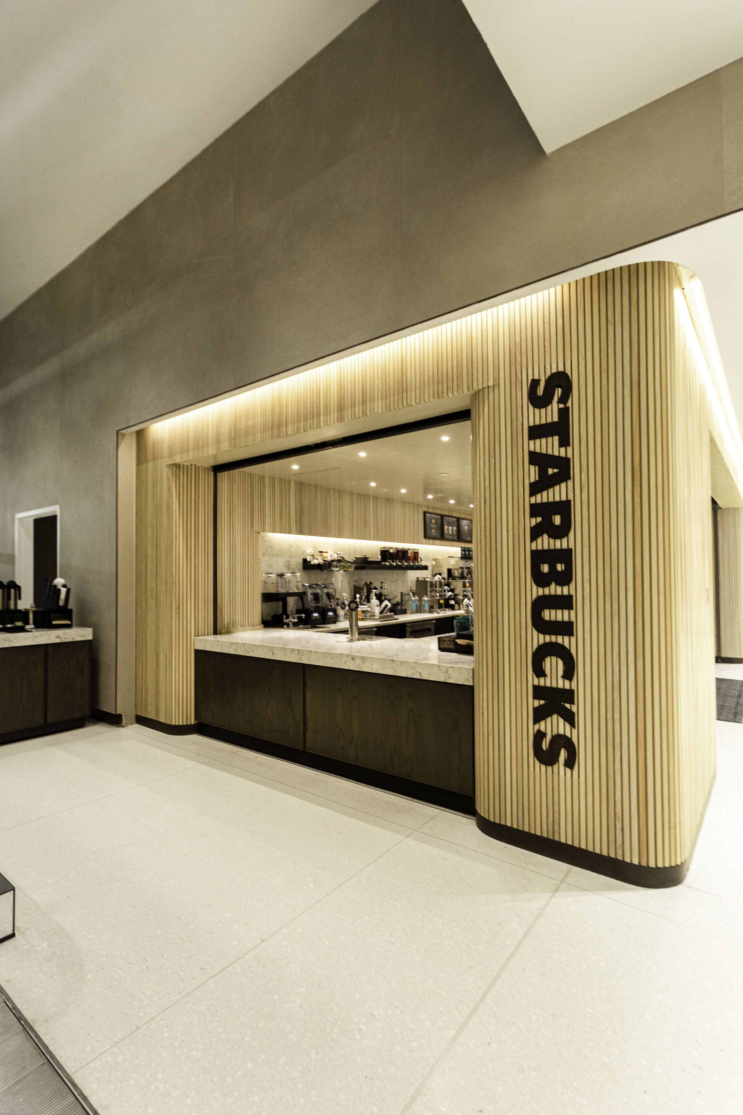 Una tienda Starbucks moderna con un diseño minimalista, que presenta un letrero grande iluminado y un interior limpio y contemporáneo.