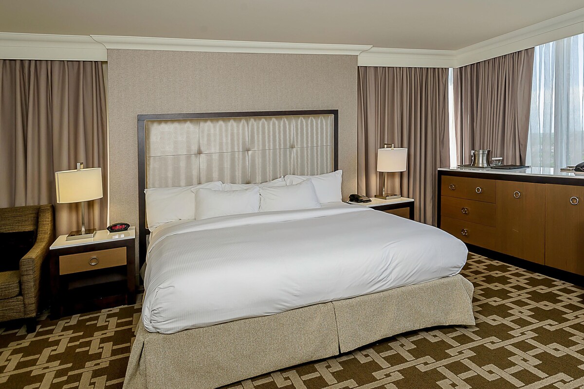 A hotel room with a large bed, a nightstand, a desk, a chair, and a window with curtains.