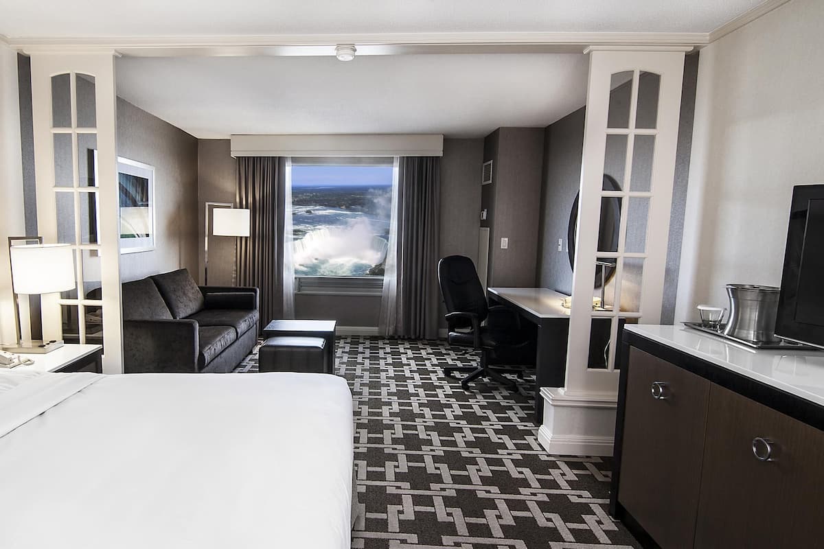 Une chambre d’hôtel équipée d’un lit, d’un bureau, d’une chaise, d’un canapé, d’une télévision, d’une lampe et offrant une vue sur une cascade.