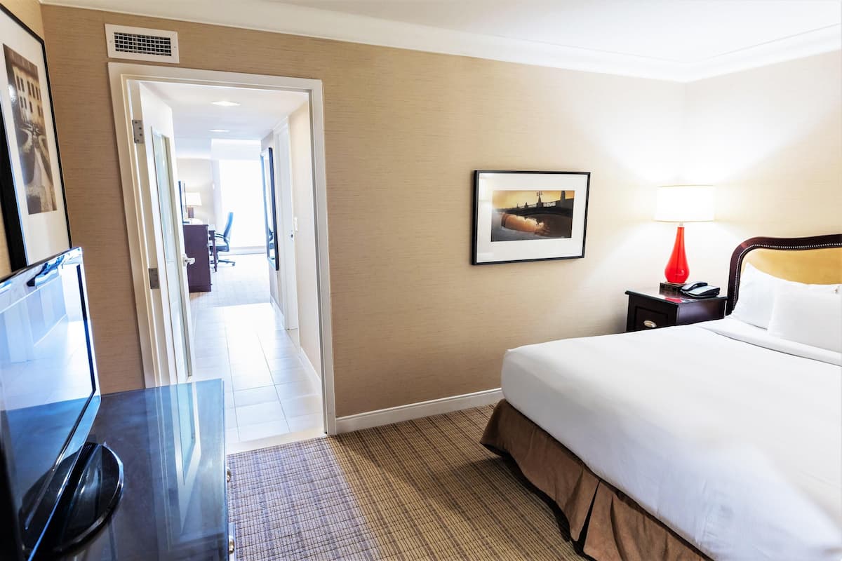 Une chambre d’hôtel avec un lit, un bureau équipé d’un ordinateur, une lampe et un tableau encadré au mur.