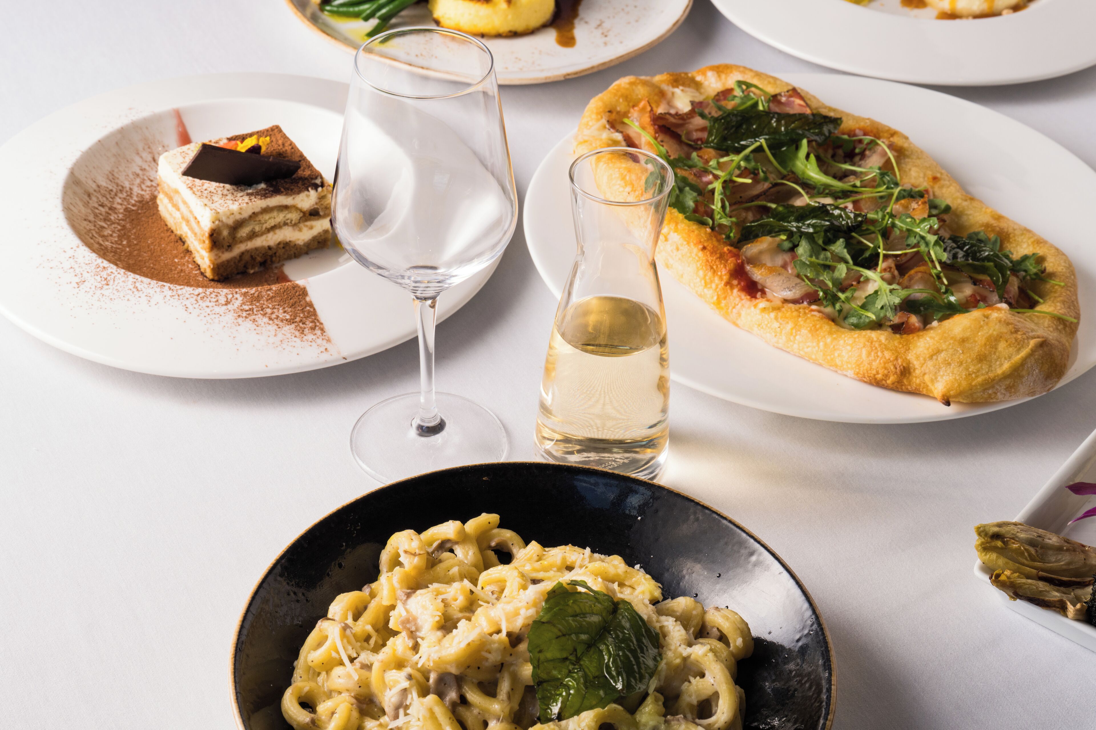 A dining table with various dishes including pasta, pizza, and a dessert.