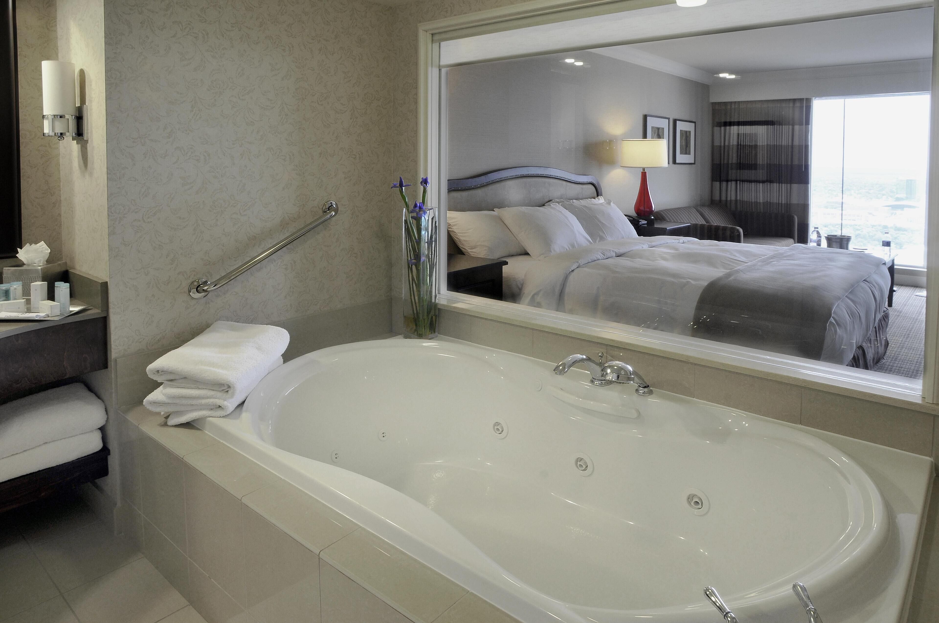 A hotel bathroom with a large bathtub, a mirror reflecting the room, and a handrail.