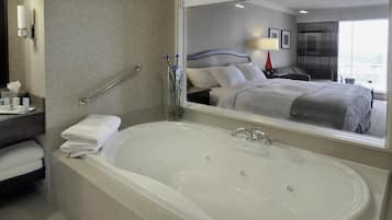 Un baño de hotel con una bañera grande, un espejo que refleja la habitación y un pasamanos.