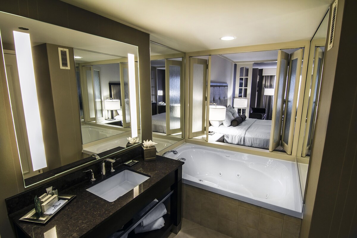 A modern bathroom with a large mirror, two sinks, a bathtub, and a toilet.