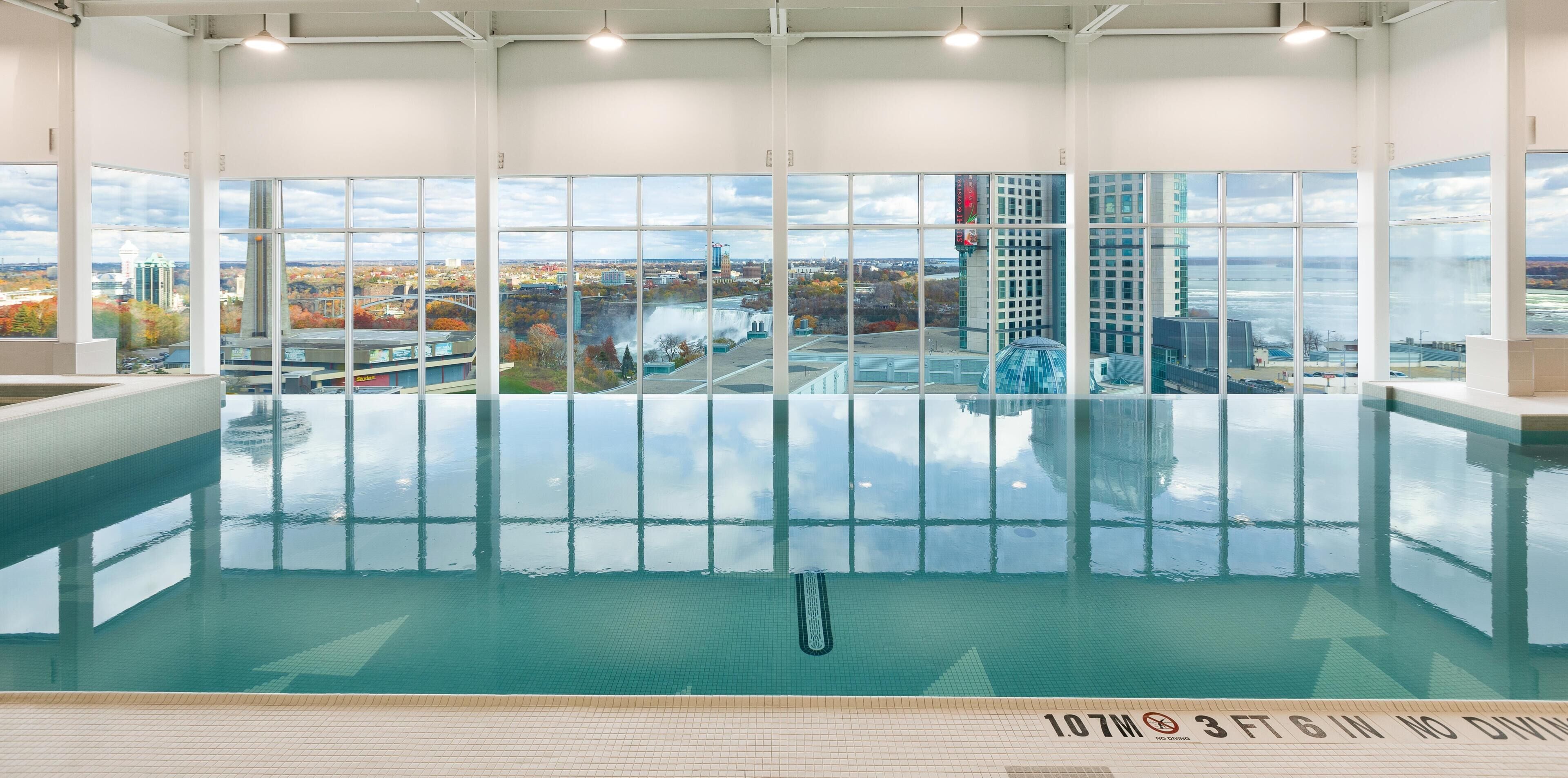 A large indoor swimming pool with a city view, clear water, and a lifeguard chair.