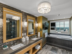 A luxurious bathroom with two sinks, a large mirror, a chandelier, a television, and a bathtub.