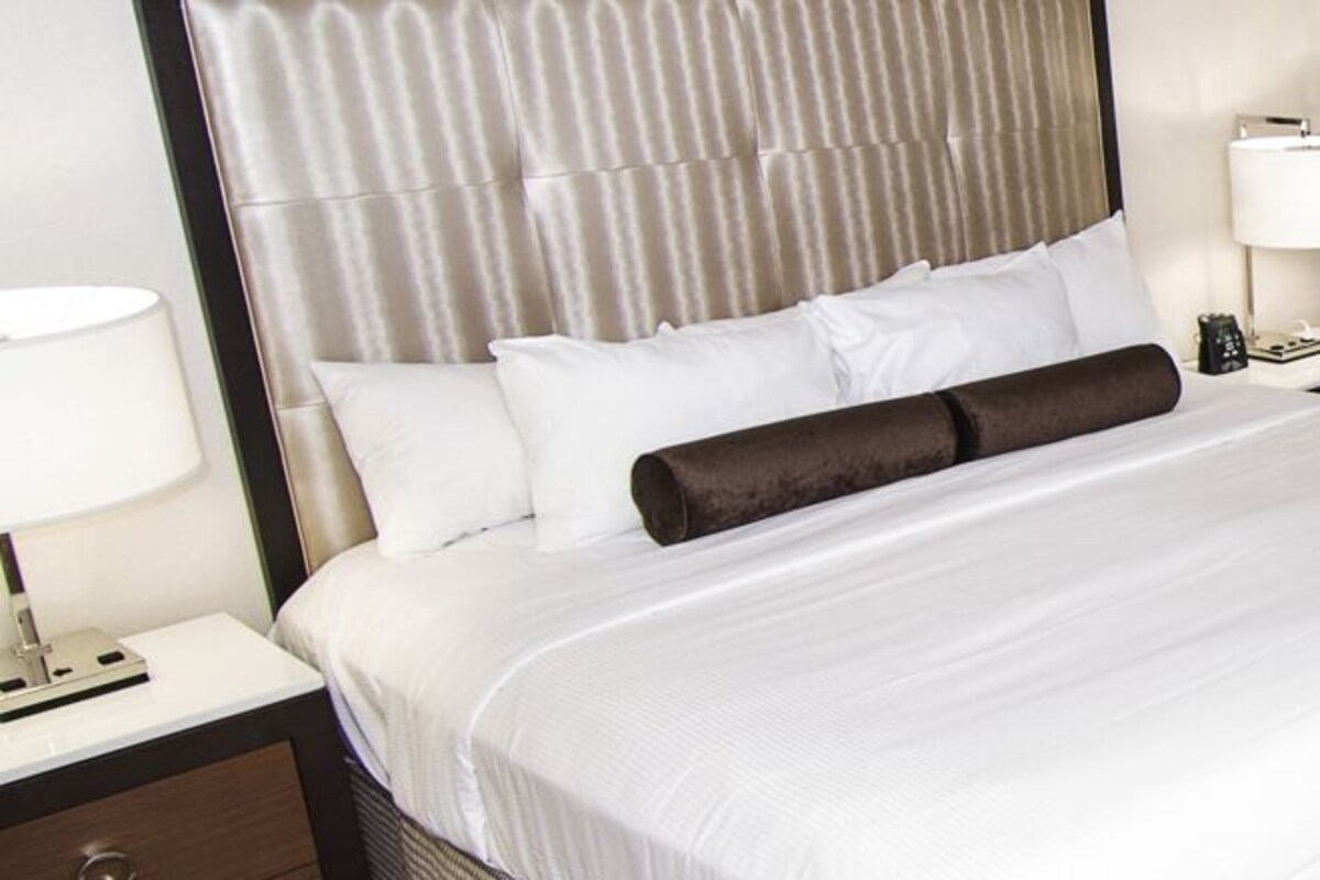 Un lit bien fait, avec du linge de lit blanc, un coussin décoratif de couleur marron foncé et une tête de lit ornée de motifs verticaux.