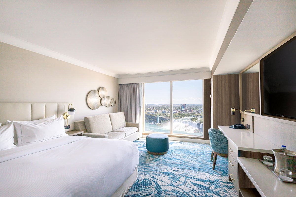 A hotel room with a large bed, a sofa, a desk, and a TV.