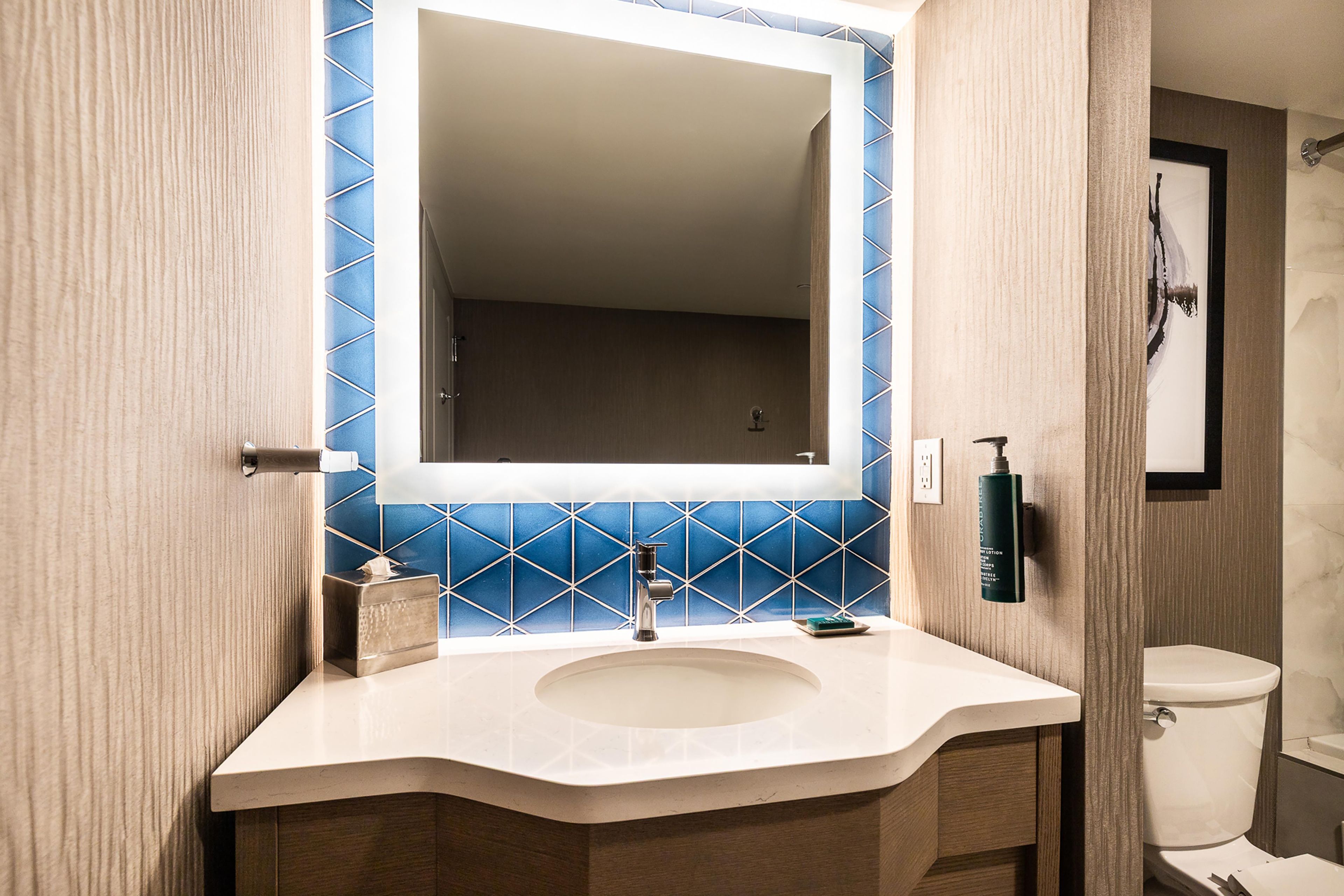 A bathroom with a white sink, a mirror, and blue-tiled walls.