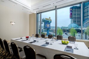 A conference room with a large table, chairs, and a view of a cityscape through large windows.